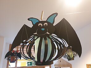 Ein Bild von einer von Kindern gebastelten, schwarzen Fledermaus, mit Fangzähnen und einem blauen Bauch.